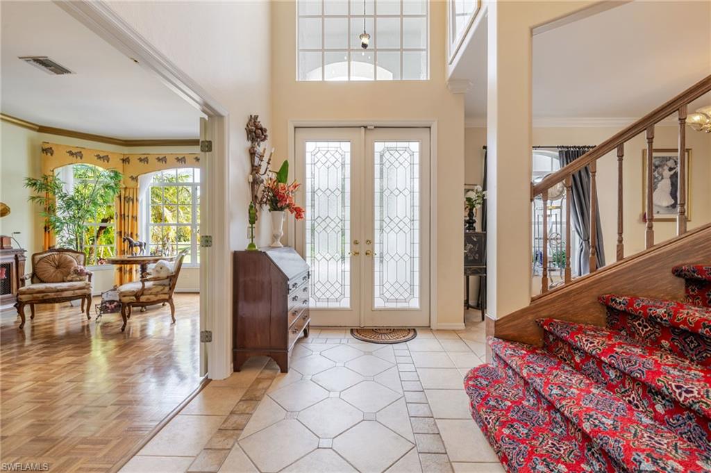 Entryway featuring crown molding, french doors, light tile patterned floors, inlaid floor details, and a high ceiling