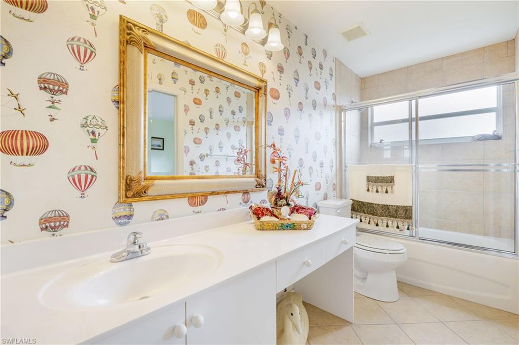 Bathroom featuring combined bath / shower with glass door, light tile patterned floors, vanity, and wallpapered walls