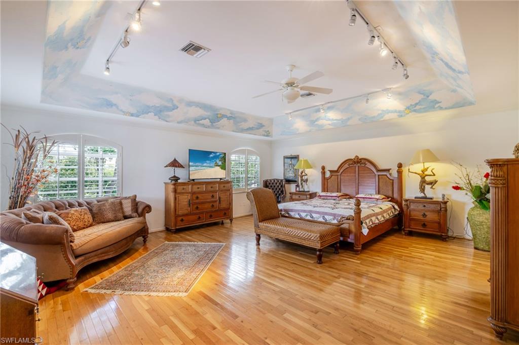Bedroom with track lighting, a raised ceiling, light wood-style floors, and ceiling fan