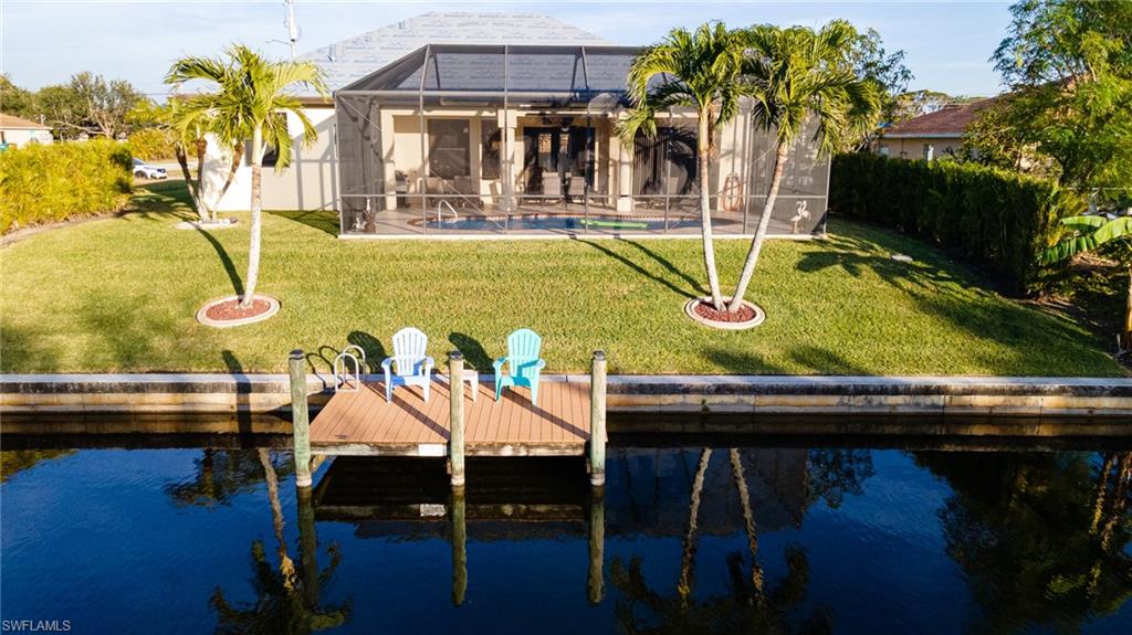 Back of house featuring a lawn, a sunroom, glass enclosure, and a water view