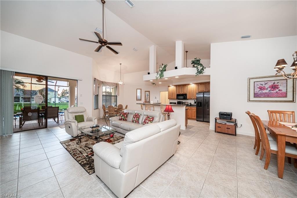 Living room featuring a chandelier, high vaulted ceiling, light tile patterned flooring, and a ceiling fan