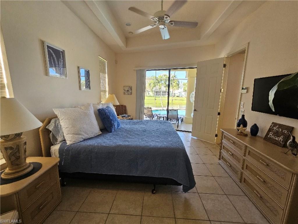 Bedroom featuring light tile patterned flooring, a raised ceiling, access to exterior, and a ceiling fan