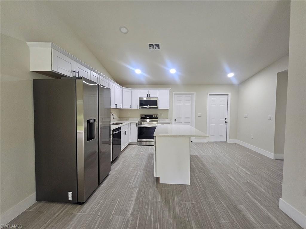Kitchen featuring stainless steel appliances, white cabinetry, recessed lighting, a kitchen island, and lofted ceiling