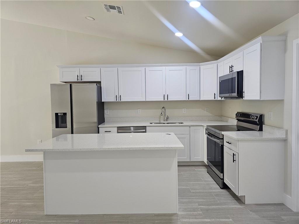 Kitchen featuring appliances with stainless steel finishes, white cabinetry, light stone counters, vaulted ceiling, and recessed lighting