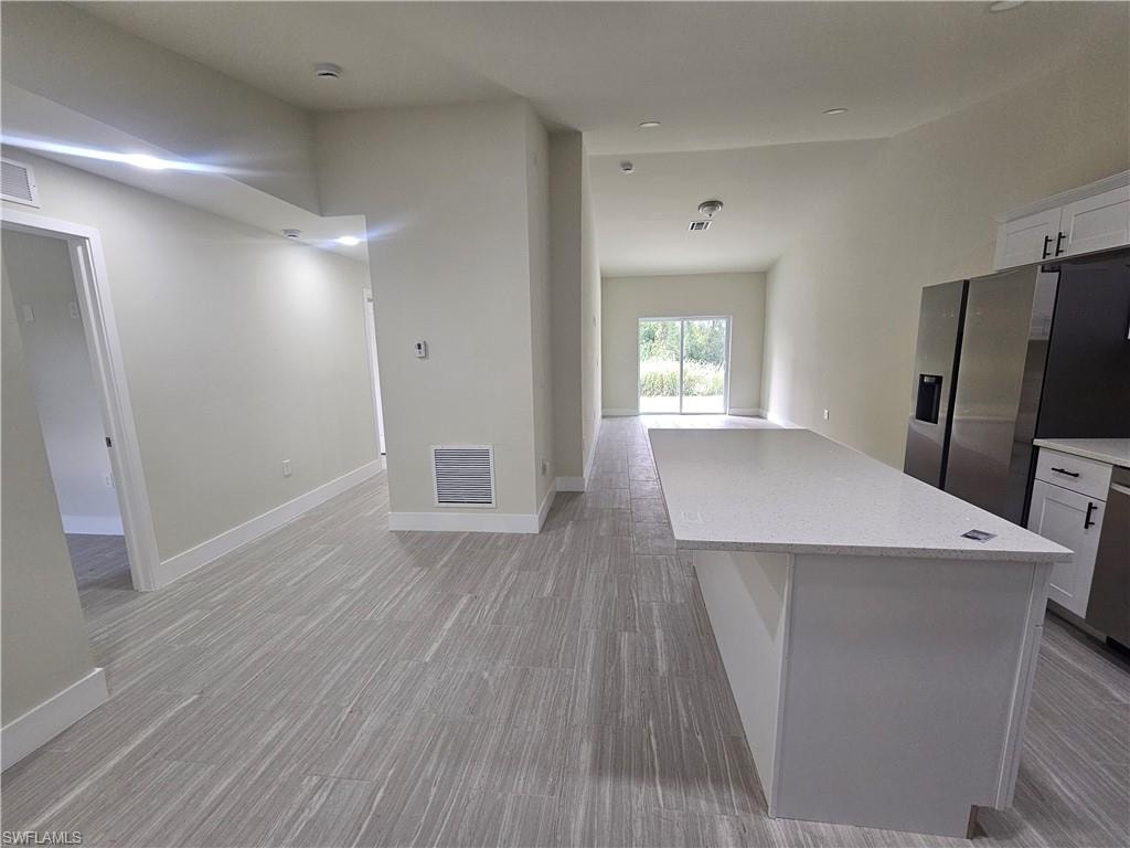 Kitchen featuring white cabinets, stainless steel appliances, light stone counters, and open floor plan