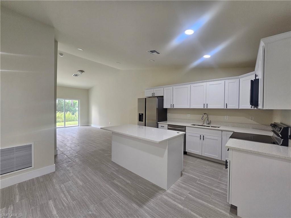 Kitchen with lofted ceiling, a center island, white cabinets, stainless steel appliances, and open floor plan