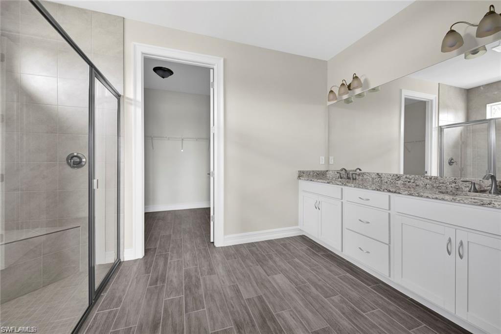 Bathroom with a walk in closet, a shower stall, double vanity, and wood tiled floors