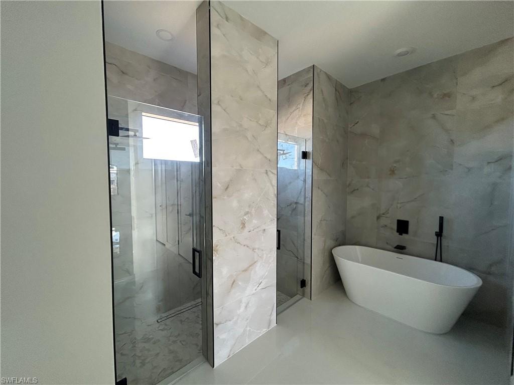 Full bathroom featuring a marble finish shower, a freestanding bath, and tile walls