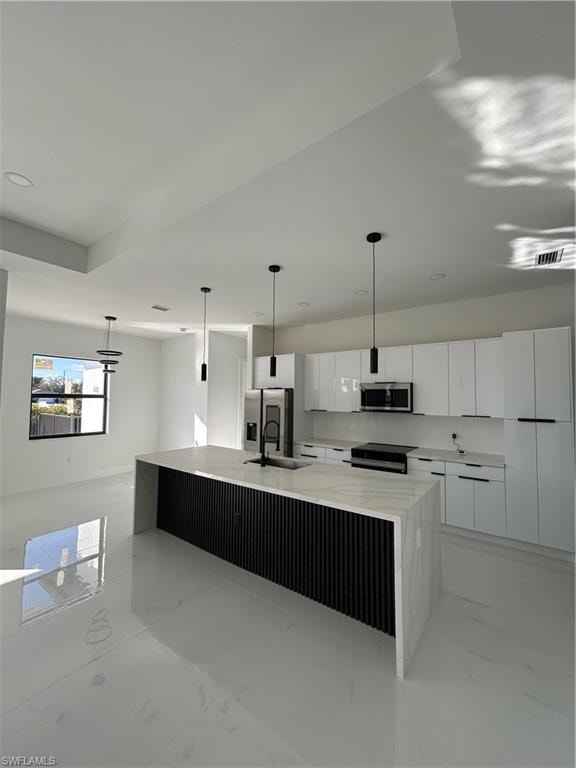 Kitchen with white cabinets, hanging light fixtures, a spacious island, light marble finish flooring, and light stone counters