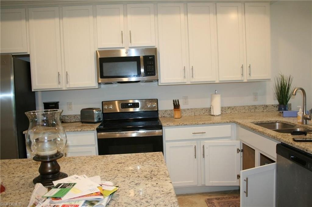Kitchen with stainless steel appliances, light stone counters, and white cabinets