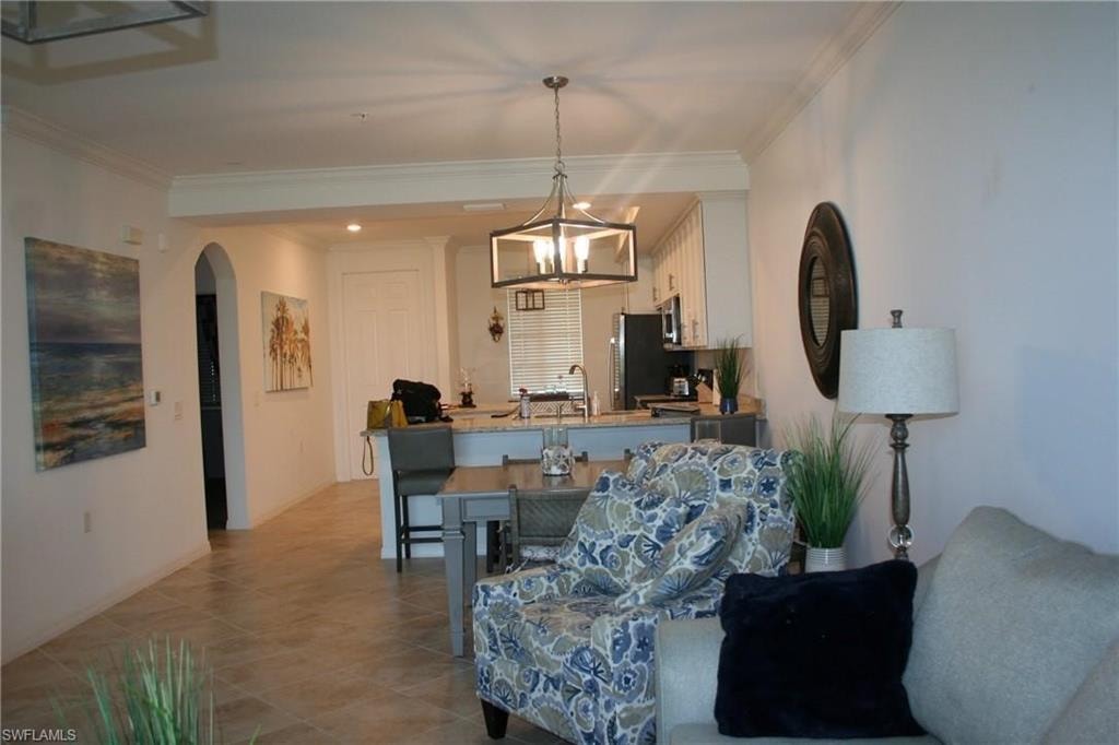 Living area featuring arched walkways, ornamental molding, light tile patterned flooring, a chandelier, and recessed lighting