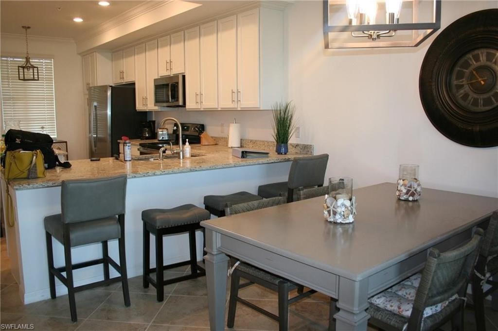 Kitchen with decorative light fixtures, white cabinetry, appliances with stainless steel finishes, a kitchen breakfast bar, and a peninsula
