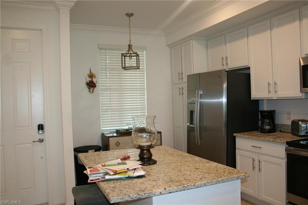 Kitchen with white cabinetry, light stone countertops, appliances with stainless steel finishes, a kitchen island, and ornamental molding