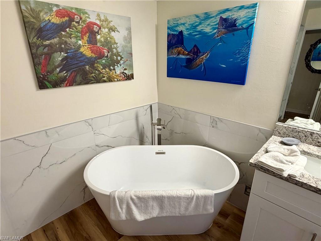 Freestanding soaking tub with floor-mounted faucet, complemented by wood-finish flooring and marble-look wall tile