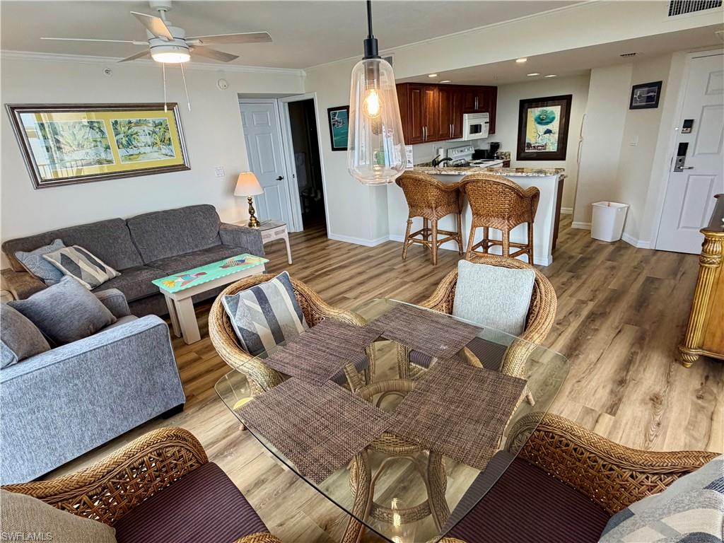 Open-concept living space featuring wood-finish flooring, a contemporary ceiling fan, and a kitchen with rich wood cabinetry and a breakfast bar