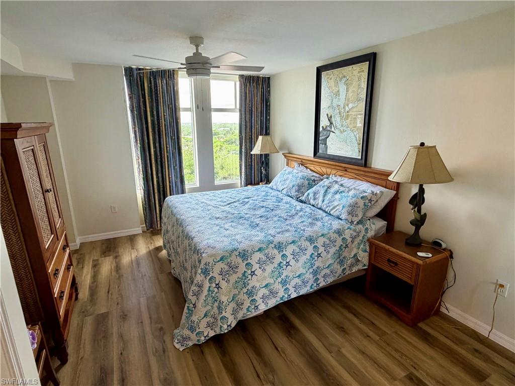 Bedroom featuring wood-finish flooring, a ceiling fan, and multiple windows with vertical blinds and patterned drapes