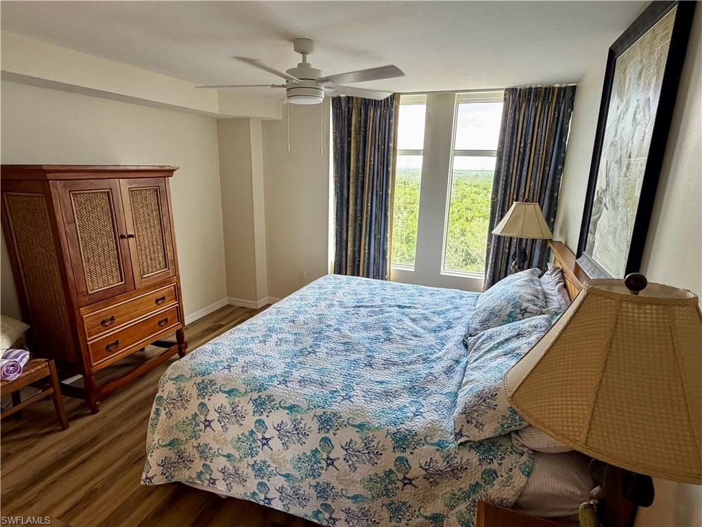 Bedroom featuring three tall windows, light wood-finish flooring, and a ceiling fan with integrated lighting