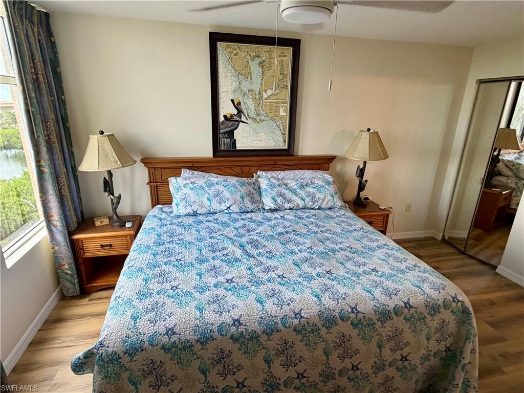 Spacious sleeping area featuring wood-finish flooring, a ceiling fan, and a large window with water scenery