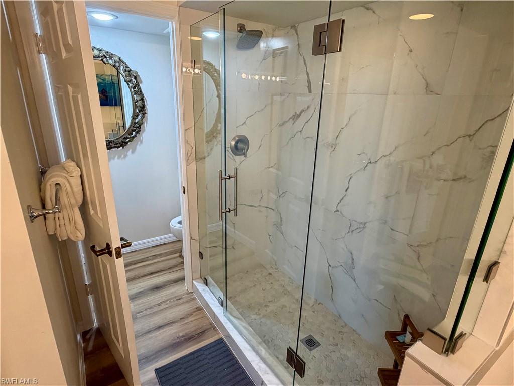 Shower enclosure featuring clear glass panels, a rainfall showerhead, and white-veined wall tiling