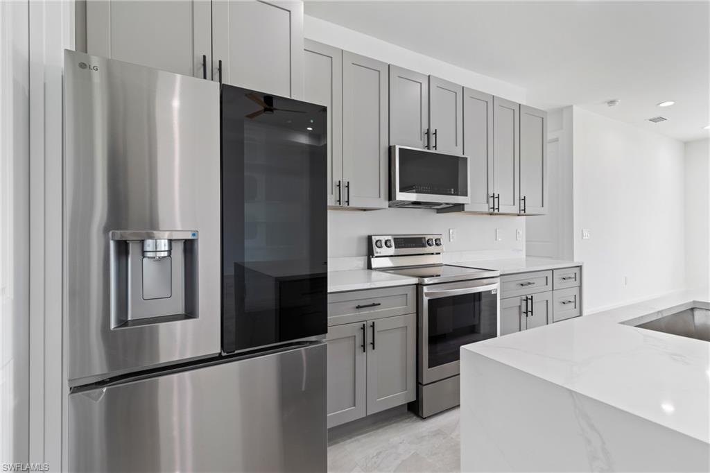 Kitchen with gray cabinets, recessed lighting, light stone countertops, visible vents, and stainless steel appliances