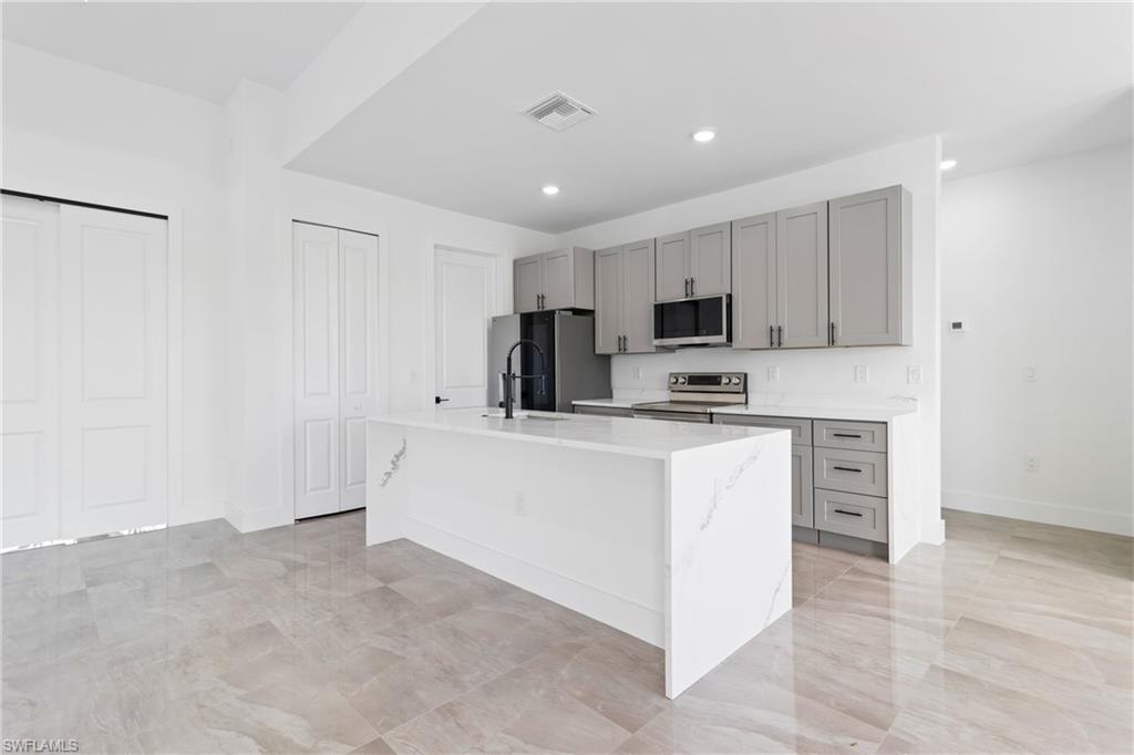 Kitchen featuring stainless steel appliances, visible vents, a center island with sink, and gray cabinets