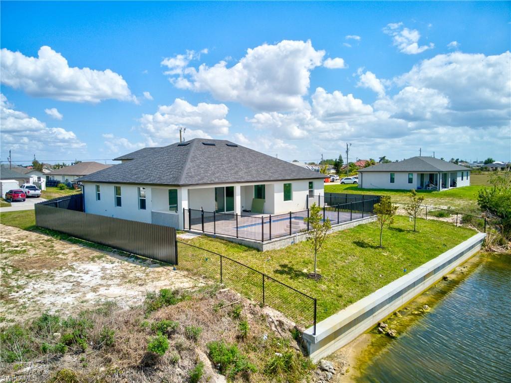 Rear view of property featuring stucco siding, a fenced backyard, a water view, a shingled roof, and a lawn