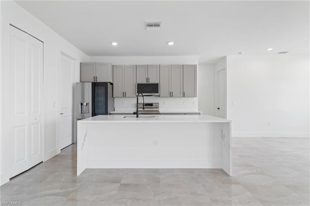 Kitchen with an island with sink, light countertops, gray cabinetry, visible vents, and stainless steel appliances