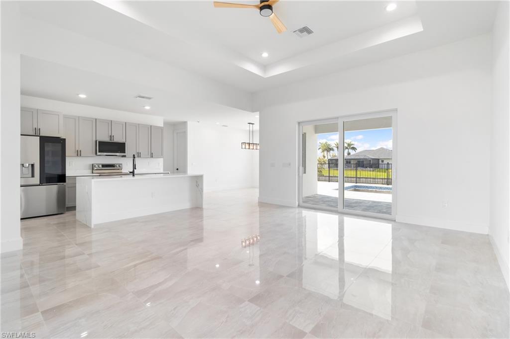 Unfurnished living room featuring visible vents, ceiling fan, a tray ceiling, and baseboards