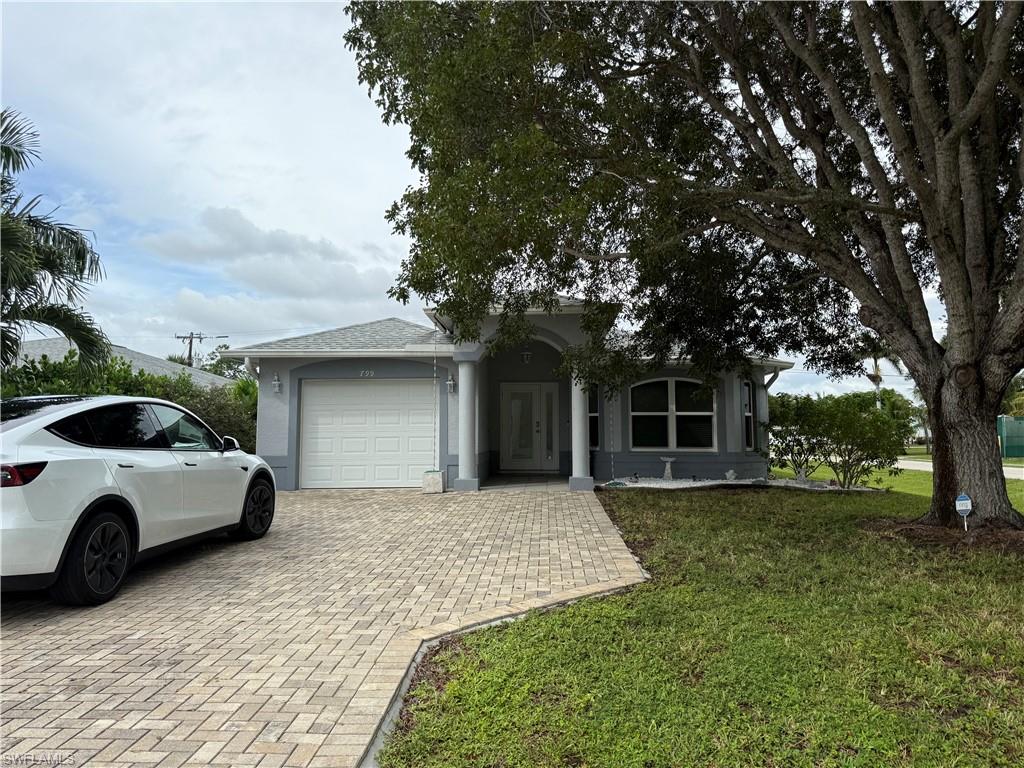 View of front of property with a garage, decorative driveway, a front lawn, and stucco siding