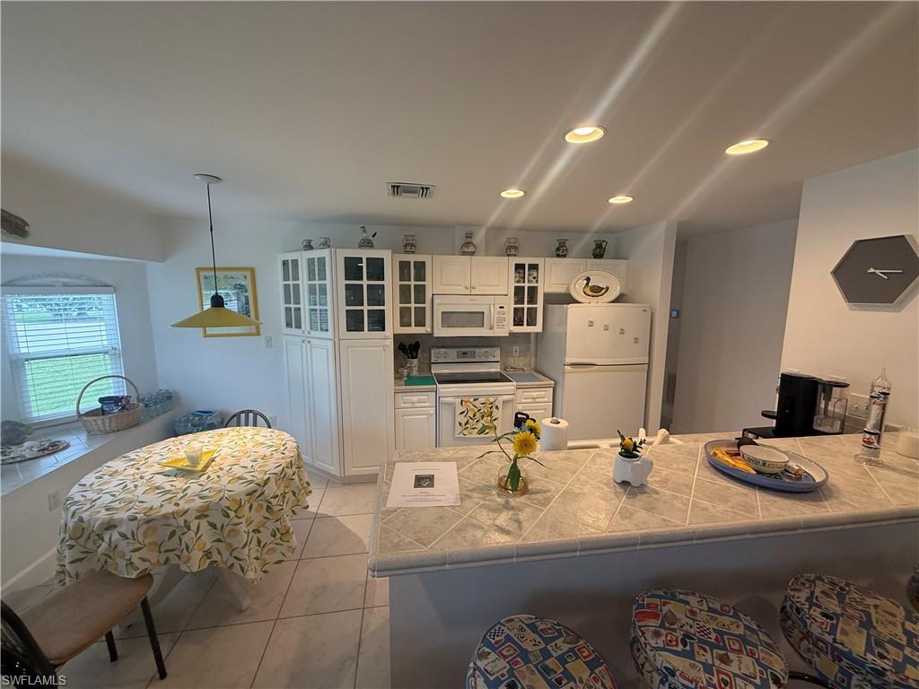 Kitchen with a breakfast bar area, white appliances, white cabinets, light tile patterned floors, and glass insert cabinets
