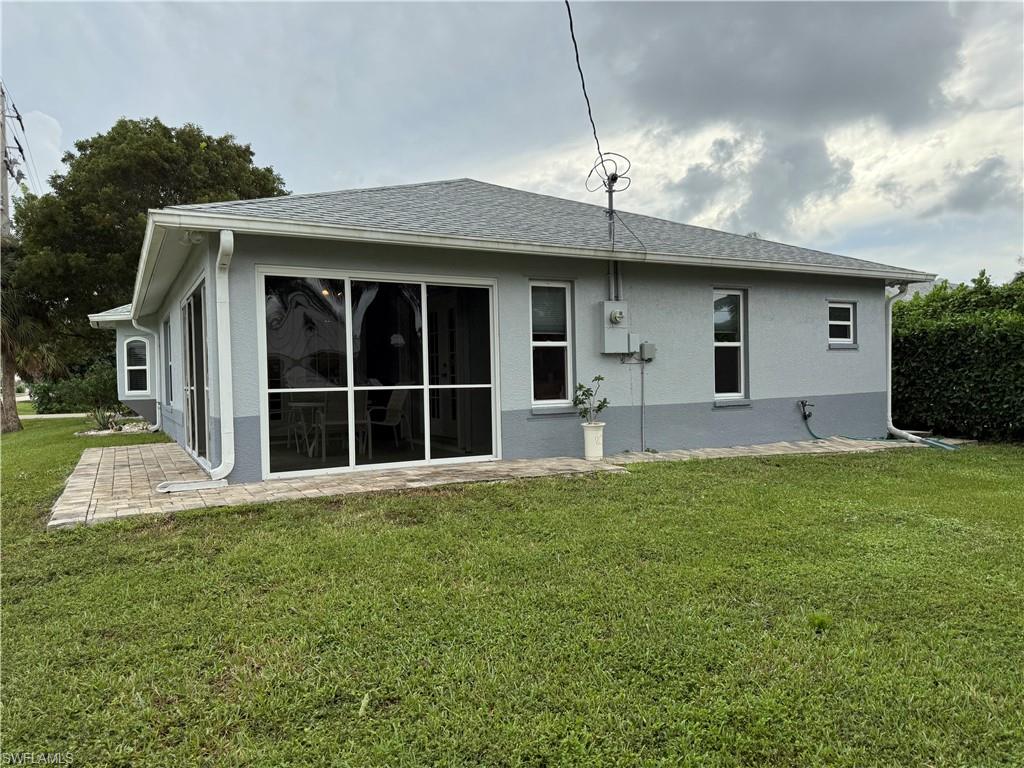 Back of house featuring a lawn, stucco siding, and a sunroom