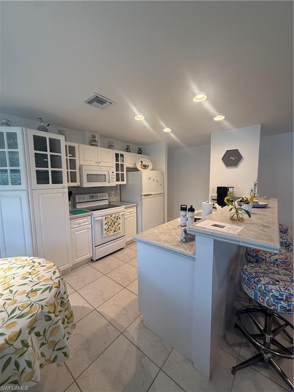 Kitchen with range, a breakfast bar, white cabinets, white fridge, and recessed lighting