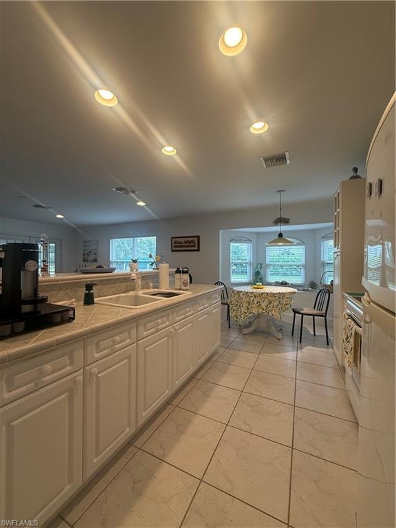 Kitchen with tile countertops, white appliances, decorative light fixtures, white cabinetry, and glass insert cabinets