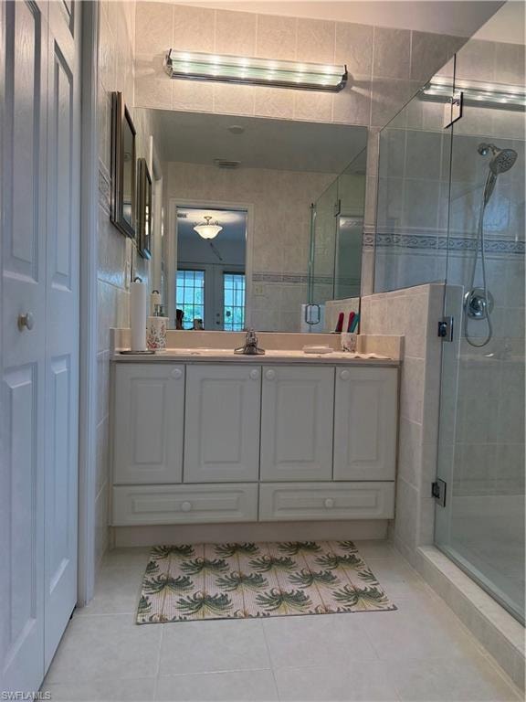 Full bathroom with a shower stall, light tile patterned flooring, vanity, tile walls, and a closet