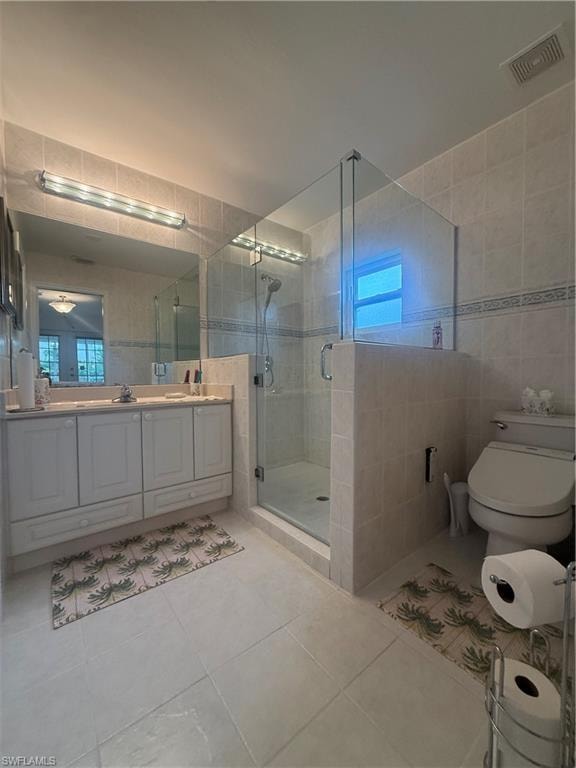 Bathroom featuring tile walls, double vanity, a shower stall, light tile patterned floors, and a closet
