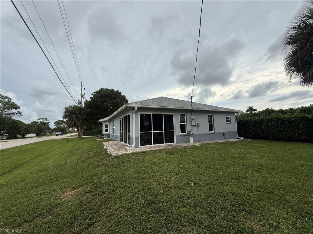 Back of house with a lawn, stucco siding, a sunroom, and roof with shingles