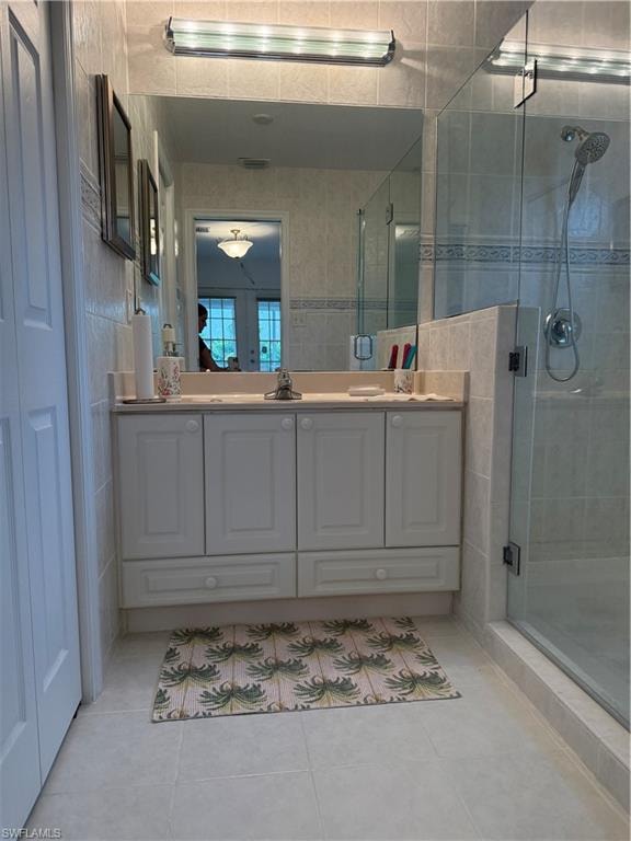 Full bathroom featuring tile walls, double vanity, a shower stall, and light tile patterned floors