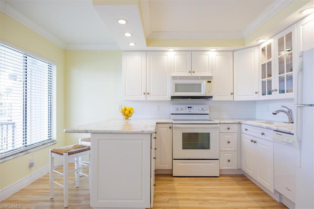Kitchen featuring recessed lighting, ornamental molding, white appliances, a peninsula, and white cabinetry