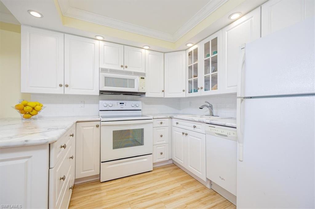 Kitchen with white appliances, white cabinets, ornamental molding, recessed lighting, and glass insert cabinets