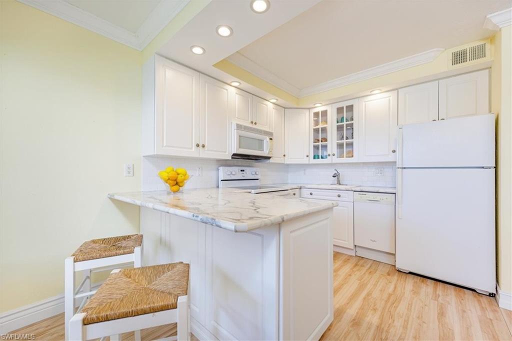 Kitchen featuring white appliances, backsplash, ornamental molding, white cabinets, and light wood-style flooring