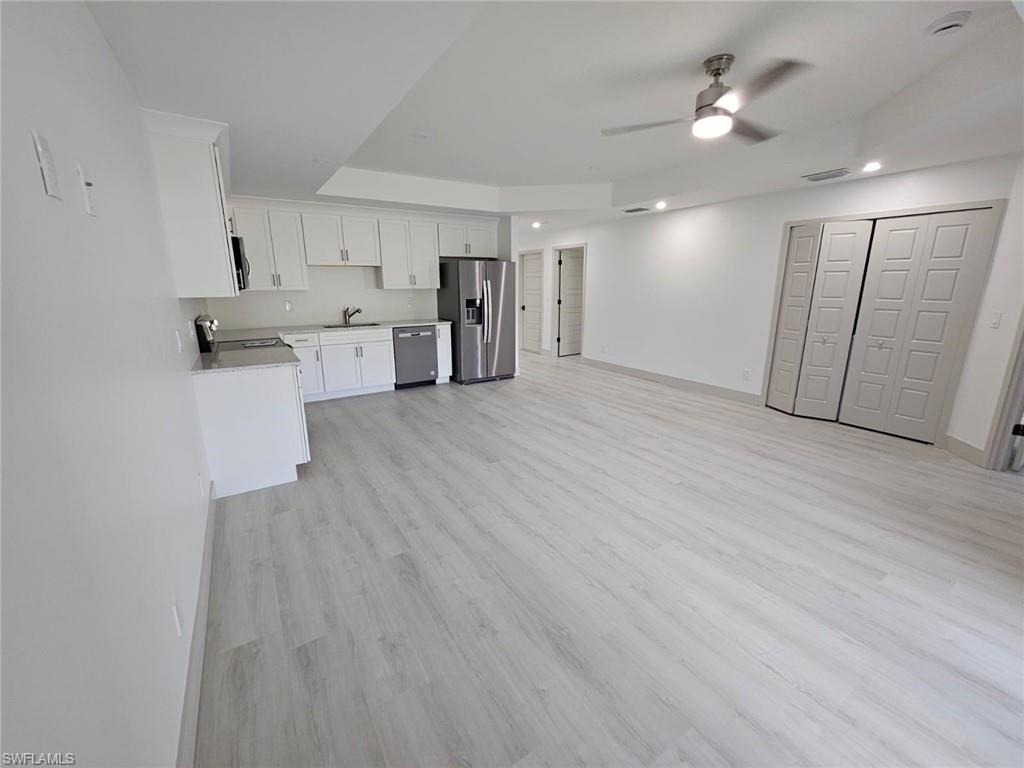 Kitchen featuring light wood finished floors, white cabinets, stainless steel appliances, open floor plan, and a ceiling fan