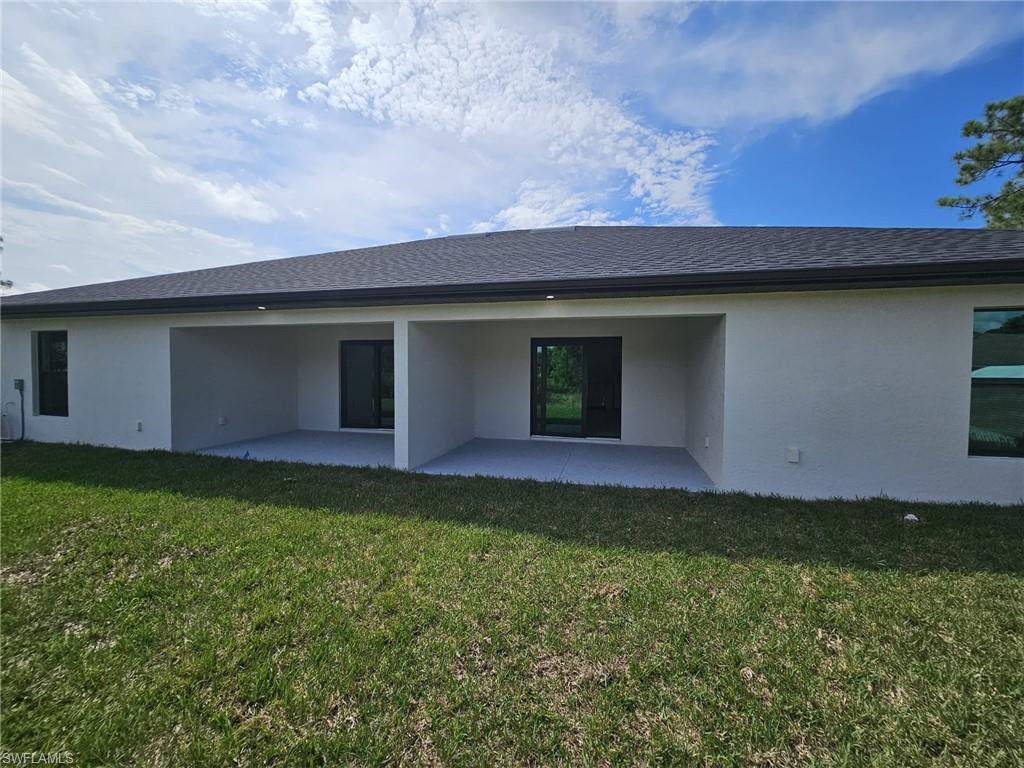 Rear view of property with stucco siding, a patio area, a yard, and a shingled roof