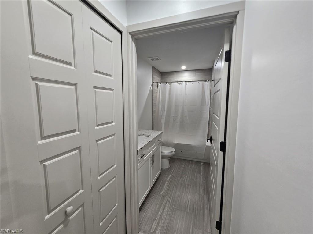 Bathroom featuring shower / tub combo with curtain, vanity, and dark wood-type flooring
