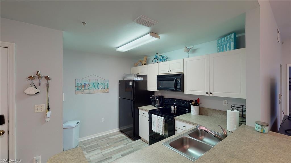 Kitchen with black appliances, white cabinetry, light countertops, and light wood-type flooring