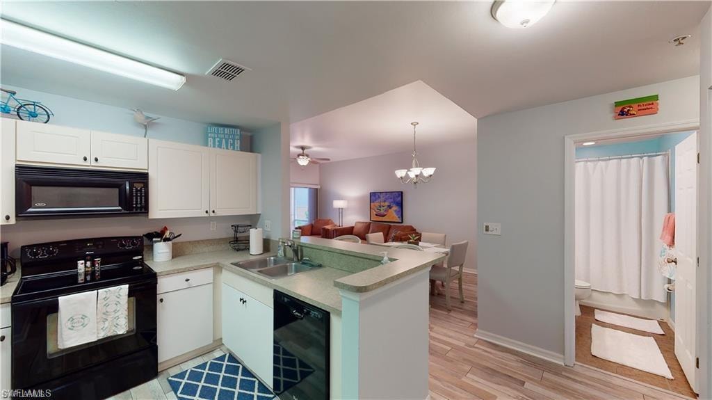 Kitchen with black appliances, a chandelier, white cabinetry, light countertops, and a peninsula