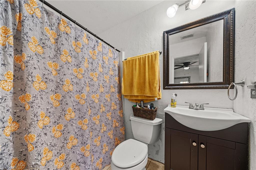 Full bathroom featuring a textured wall, a shower with shower curtain, vanity, and ceiling fan