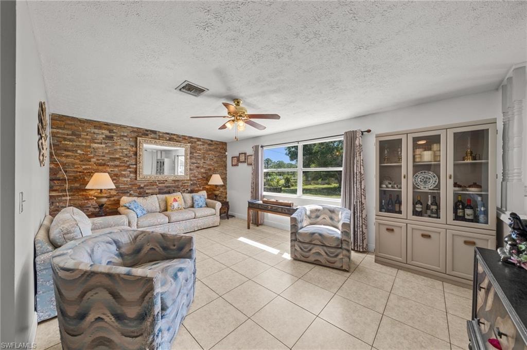 Living area featuring a textured ceiling, light tile patterned flooring, and ceiling fan