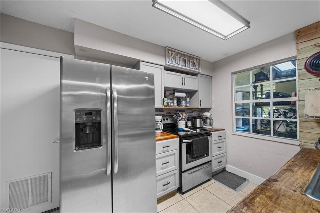 Kitchen featuring butcher block counters, appliances with stainless steel finishes, light tile patterned floors, open shelves, and white cabinets