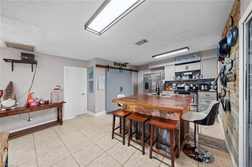 Kitchen featuring a barn door, a textured ceiling, appliances with stainless steel finishes, white cabinets, and light tile patterned flooring