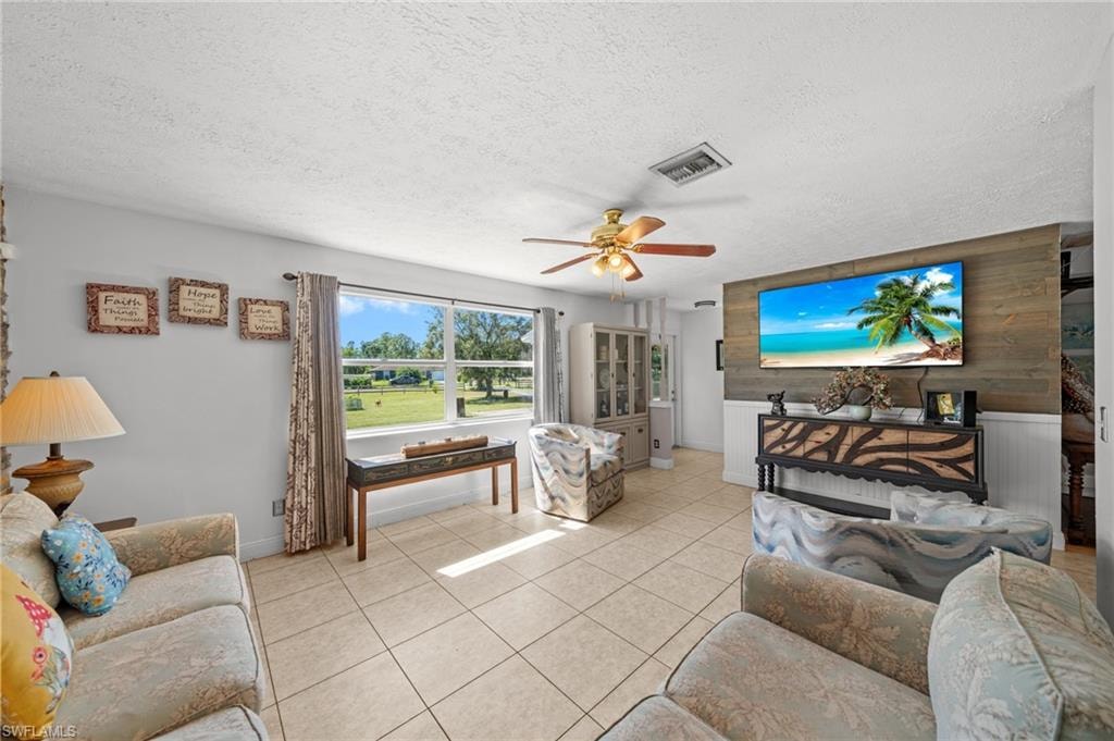 Living area with tile patterned flooring, a textured ceiling, ceiling fan, and wooden walls
